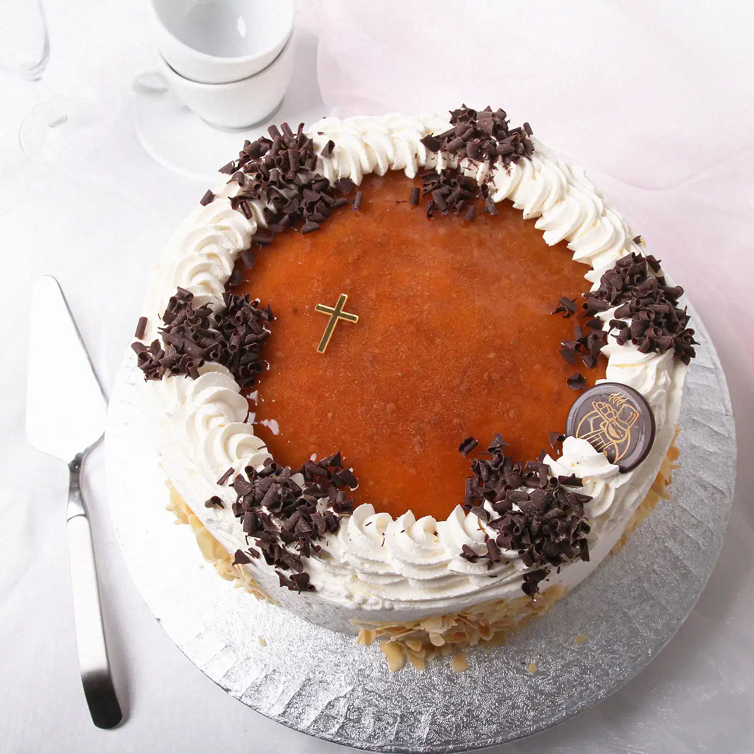 Kultaisella ristillä ja kermavaahdolla koristeltu lakkatäytekakku